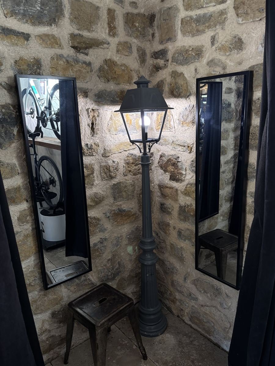Cabine d’essayage avec un réverbère, des miroirs et un tabouret devant un mur en pierre