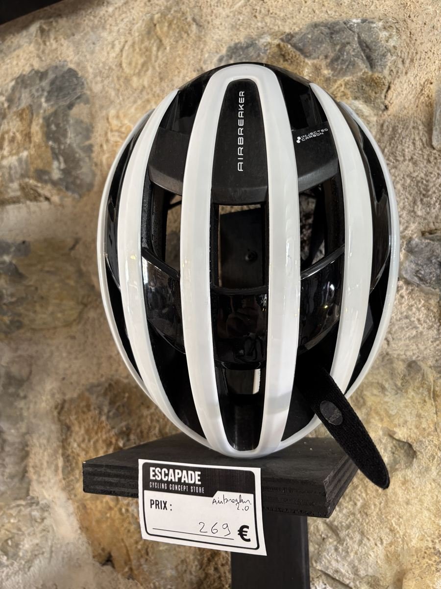 Casque de vélo blanc sur un présentoir, devant un mur en pierre